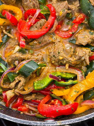 Steak Fajitas filling with marinated beef strips, multicoloured bell peppers, poblano peppers, and jalapeno in a skillet.