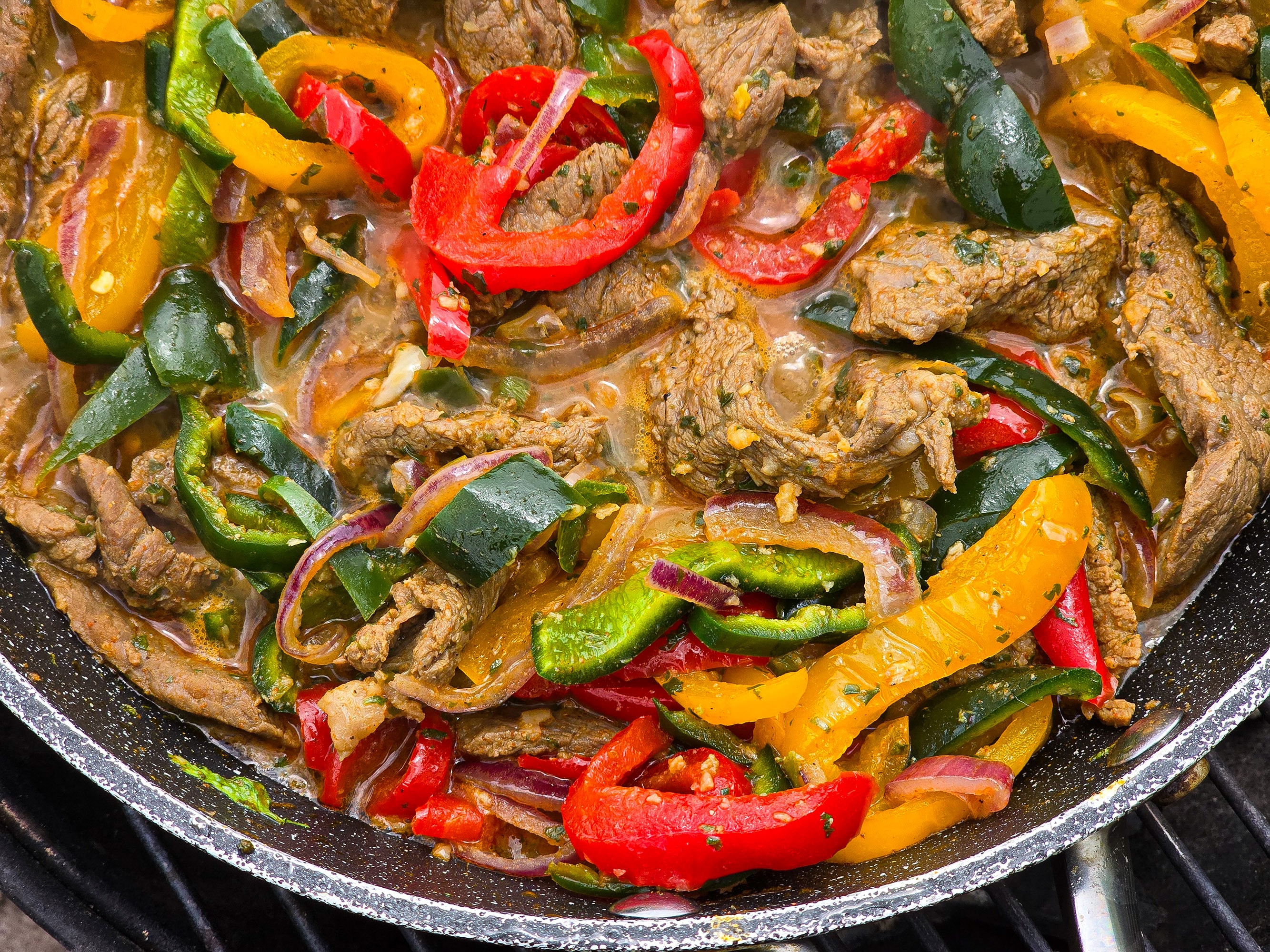 Steak Fajitas filling with marinated beef strips, multicoloured bell peppers, poblano peppers, and jalapeno in a skillet.
