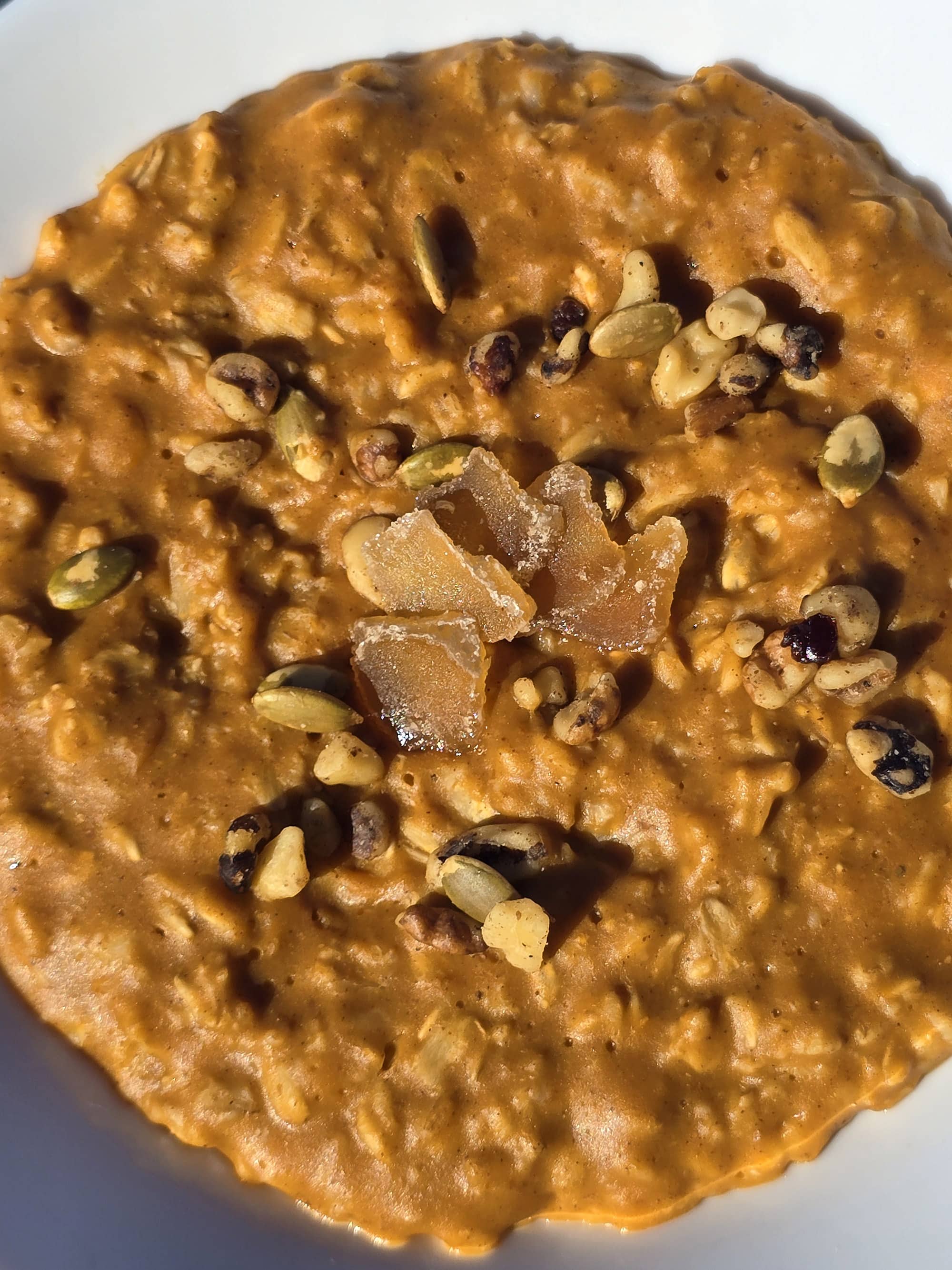 A bowl of pumpkin pie oatmeal garnished with pepitas, walnuts, and candied ginger.