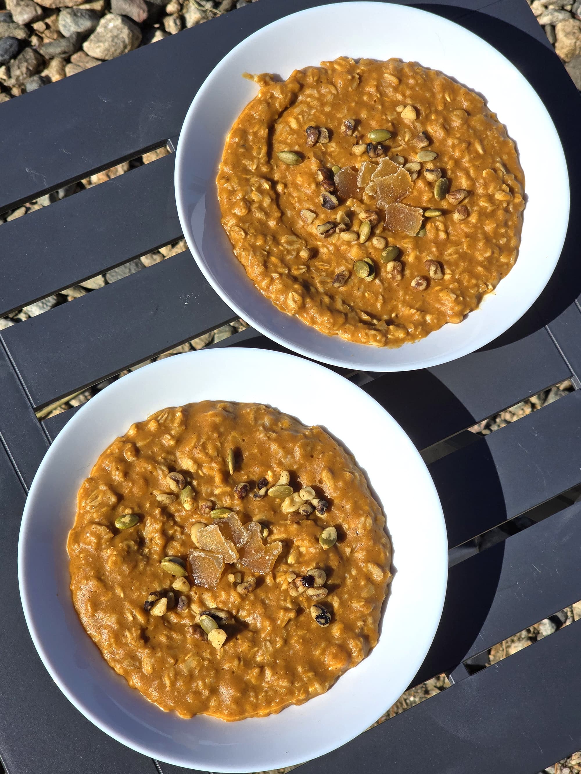 2 bowls of skillet pumpkin oatmeal garnished with pepitas, walnuts, and candied ginger.