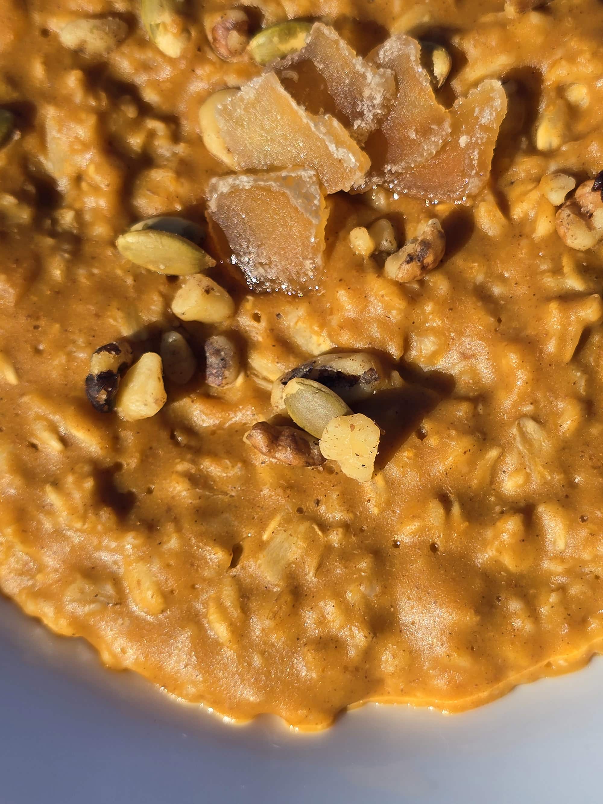 A bowl of pumpkin pie oatmeal garnished with pepitas, walnuts, and candied ginger.