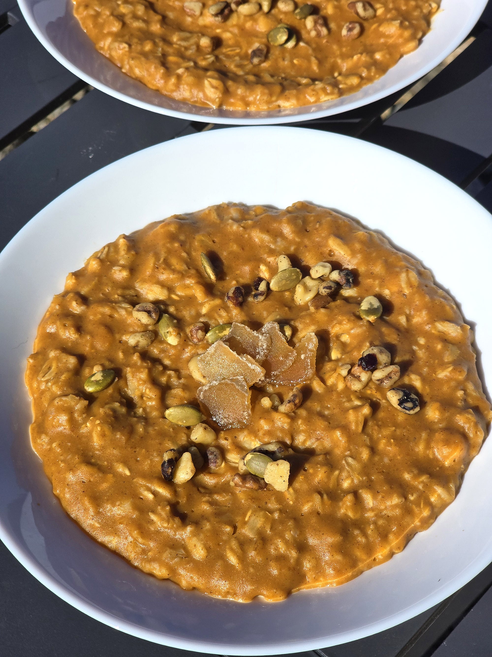 2 bowls of skillet pumpkin oatmeal garnished with pepitas, walnuts, and candied ginger.
