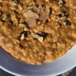 A bowl of pumpkin pie oatmeal garnished with pepitas, walnuts, and candied ginger.
