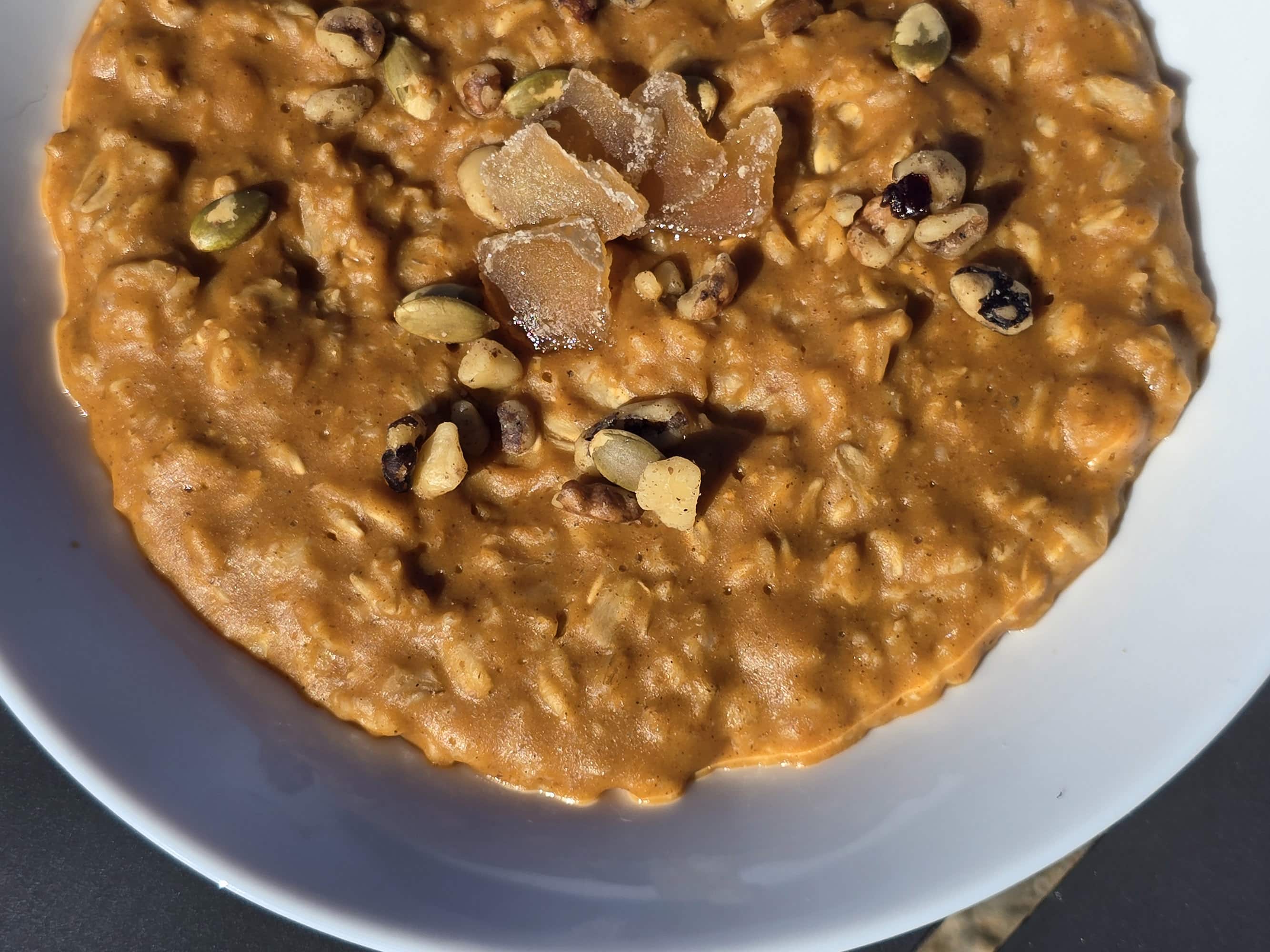 A bowl of pumpkin pie oatmeal garnished with pepitas, walnuts, and candied ginger.