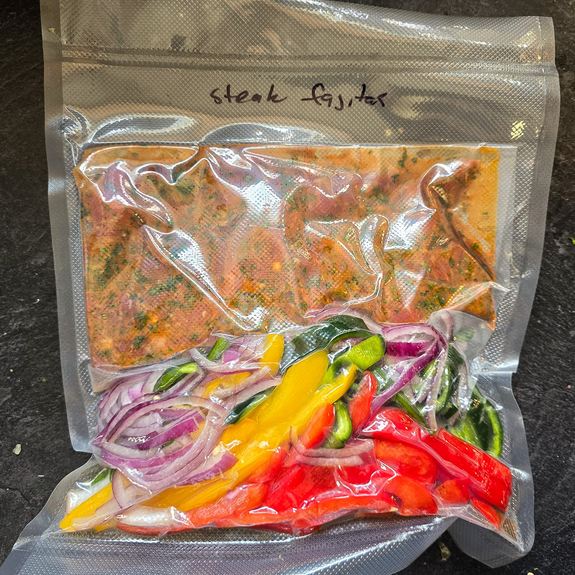 A vacuum sealed package with marinating steak and sliced peppers and onions.